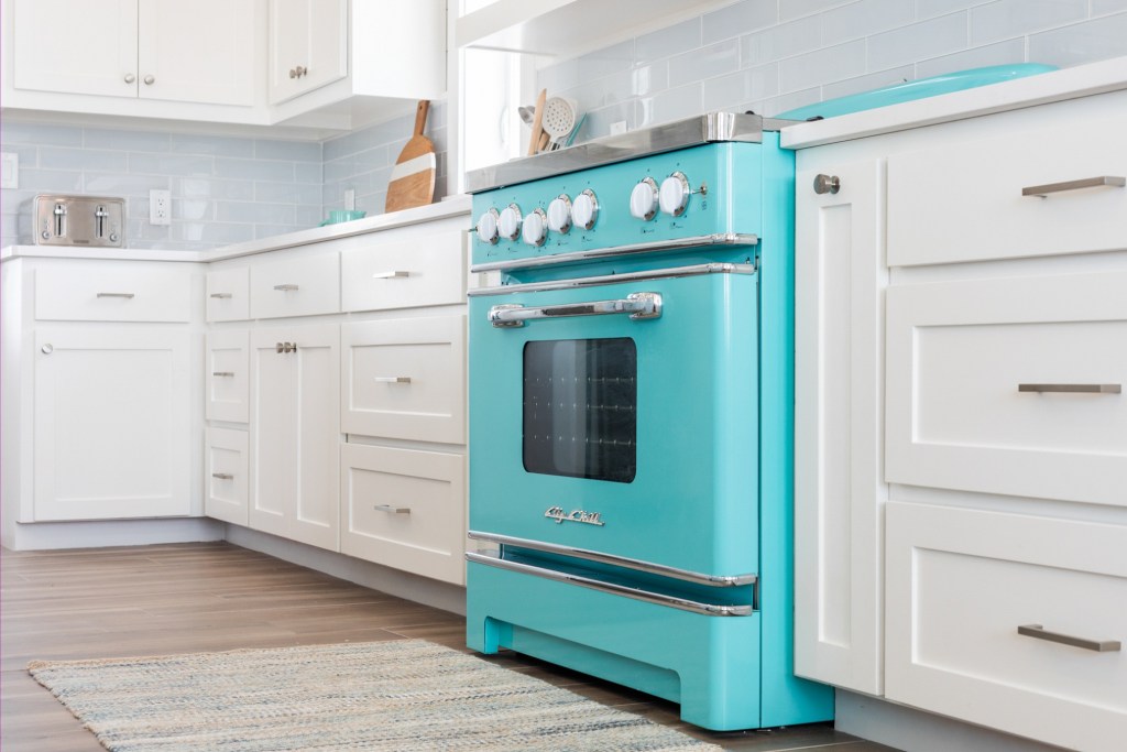A retro-style turquoise gas range in a bright, modern kitchen with white cabinetry and light blue backsplash.